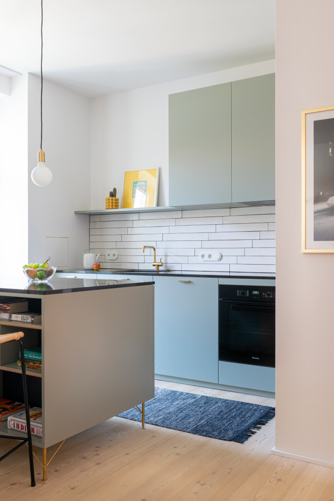 Offene, Mittelgroße Küche in L-Form mit Einbauwaschbecken, flächenbündigen Schrankfronten, grünen Schränken, Marmor-Arbeitsplatte, Küchenrückwand in Weiß, Rückwand aus Keramikfliesen, schwarzen Elektrogeräten, hellem Holzboden, Kücheninsel und schwarzer Arbeitsplatte in München