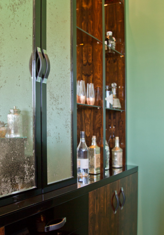This is an example of a mid-sized modern galley seated home bar in Los Angeles with no sink, medium wood cabinets, glass benchtops, black splashback, mirror splashback, medium hardwood floors, brown floor and black benchtop.
