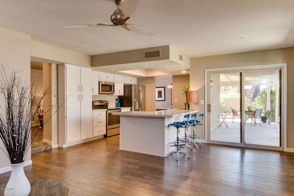Transitional medium tone wood floor and brown floor kitchen photo in Phoenix with shaker cabinets, white cabinets, stainless steel appliances and a peninsula