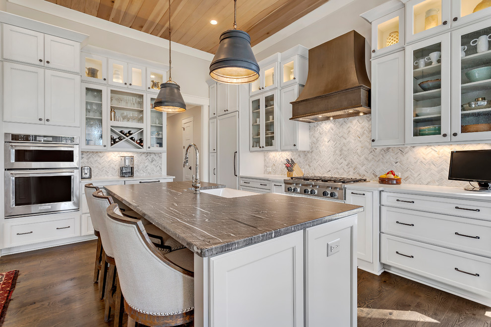 Photo of a large country l-shaped eat-in kitchen in Charleston with stainless steel appliances, dark hardwood floors, with island, brown floor, a farmhouse sink, recessed-panel cabinets, white cabinets, white splashback and mosaic tile splashback.