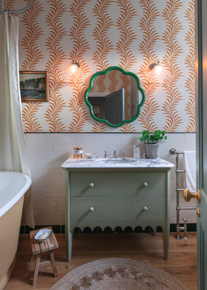 Пример оригинального дизайна: ванная комната среднего размера со стиральной машиной в стиле неоклассика (современная классика) с зелеными фасадами, отдельно стоящей ванной, душем над ванной, раздельным унитазом, белой плиткой, керамогранитной плиткой, паркетным полом среднего тона, накладной раковиной, мраморной столешницей, шторкой для ванной, тумбой под одну раковину и обоями на стенах