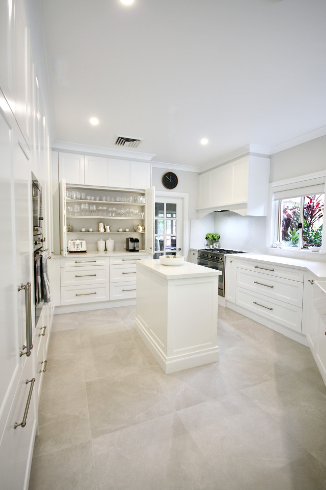 Large transitional open plan kitchen in Sydney with a farmhouse sink, recessed-panel cabinets, white cabinets, quartz benchtops, white splashback, engineered quartz splashback, stainless steel appliances, ceramic floors, with island, grey floor and white benchtop.
