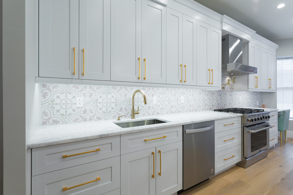 Inspiration for an expansive contemporary galley separate kitchen in New York with an undermount sink, shaker cabinets, white cabinets, quartzite benchtops, white splashback, cement tile splashback, stainless steel appliances, light hardwood floors, with island, brown floor and white benchtop.