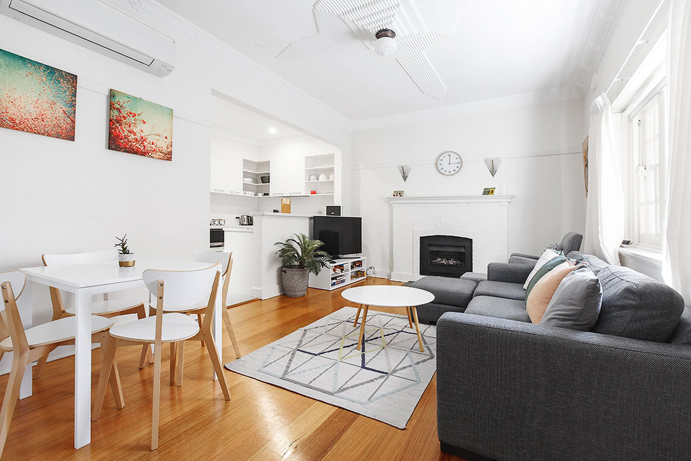 Photo of a small contemporary enclosed living room in Melbourne with white walls, medium hardwood floors, a standard fireplace, a concrete fireplace surround, a freestanding tv and brown floor.