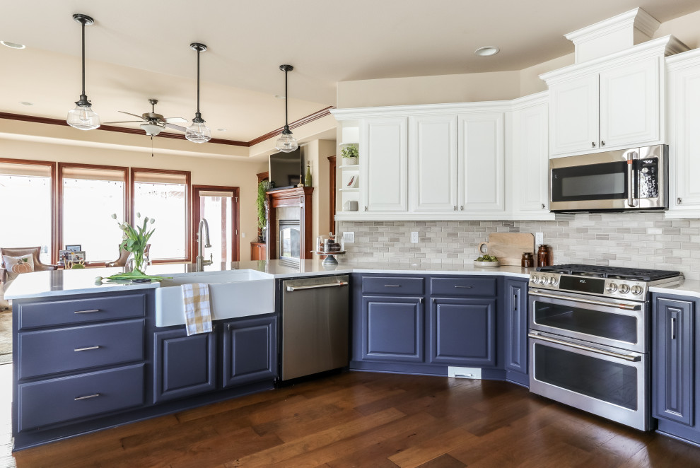 Example of a mid-sized transitional u-shaped medium tone wood floor and brown floor kitchen design in Seattle with a farmhouse sink, white cabinets, quartz countertops, gray backsplash, marble backsplash, stainless steel appliances and white countertops