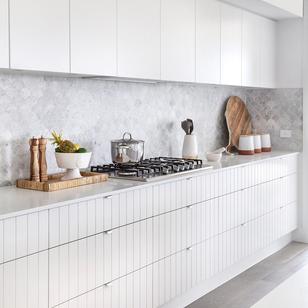 Photo of a large beach style galley kitchen pantry in Sydney with a drop-in sink, shaker cabinets, white cabinets, solid surface benchtops, glass sheet splashback, white appliances, cement tiles, multiple islands, grey floor and white benchtop.