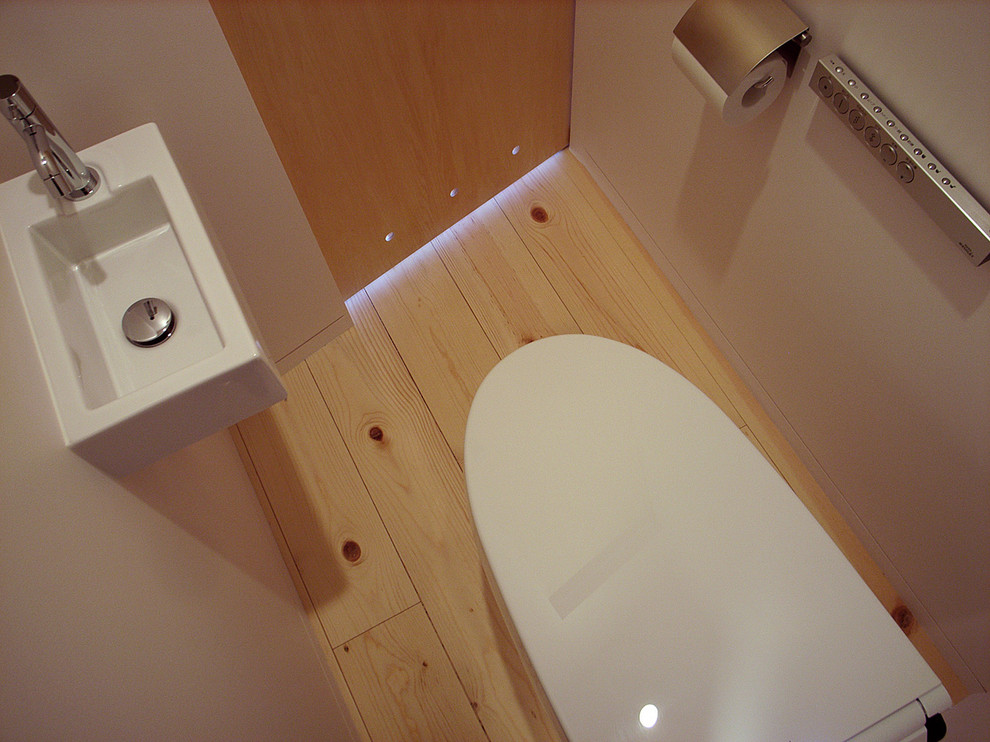 Photo of a modern powder room in Tokyo with a one-piece toilet, white tile, white walls and light hardwood floors.