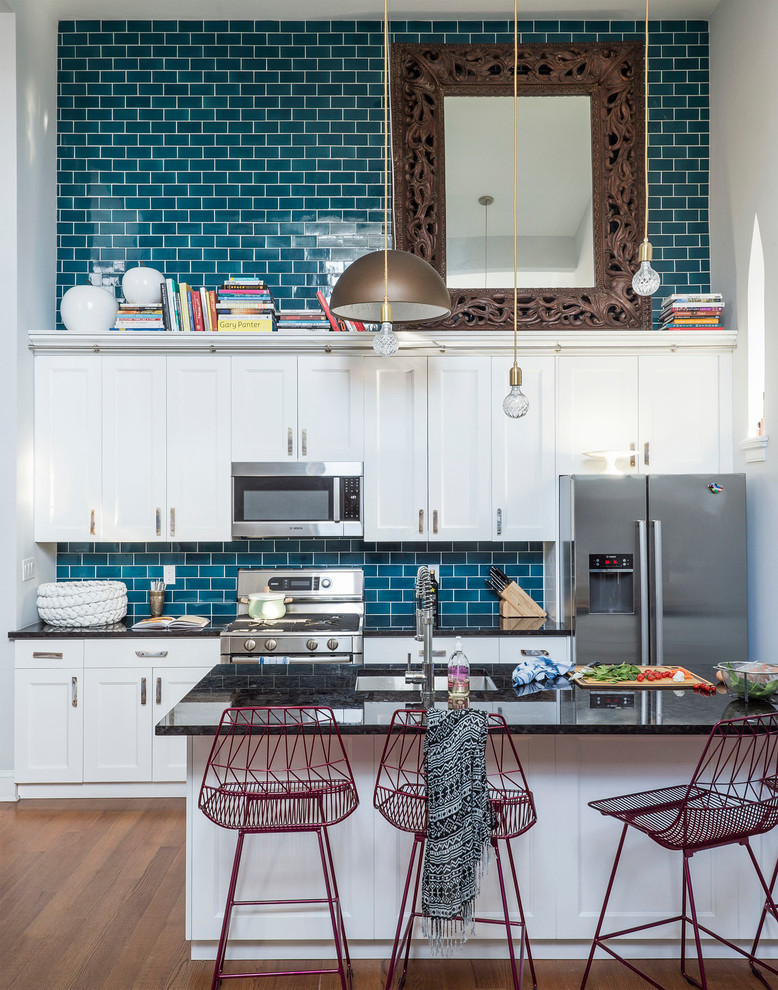 This is an example of a mid-sized eclectic galley open plan kitchen in New York with an undermount sink, shaker cabinets, white cabinets, stainless steel appliances, a peninsula, blue splashback, subway tile splashback and medium hardwood floors.