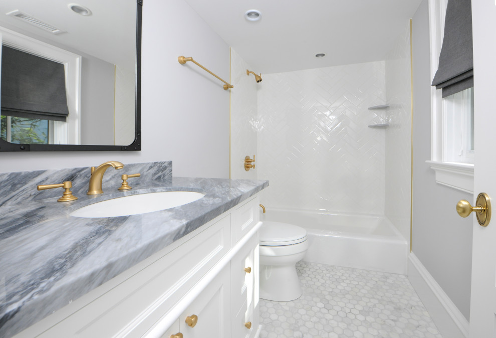 This is an example of a small contemporary kids bathroom in New York with recessed-panel cabinets, white cabinets, a drop-in tub, a shower/bathtub combo, a two-piece toilet, white tile, subway tile, grey walls, marble floors, an undermount sink, marble benchtops, grey floor, a shower curtain and blue benchtops.