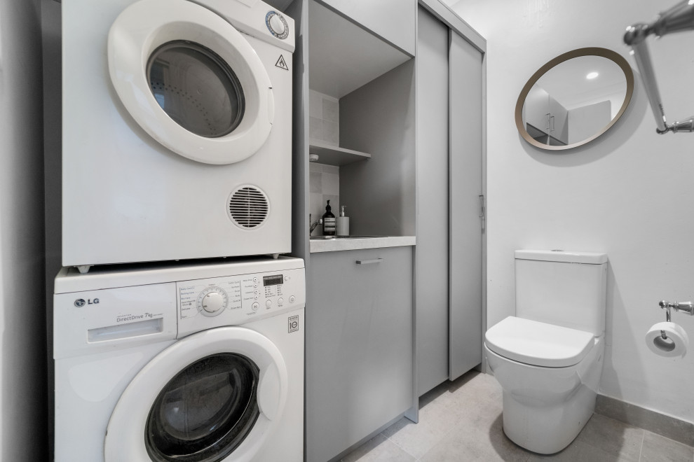 Design ideas for a mid-sized transitional single-wall utility room in Sydney with a drop-in sink, flat-panel cabinets, grey cabinets, quartz benchtops, ceramic splashback, multi-coloured walls, ceramic floors, an integrated washer and dryer, grey floor and white benchtop.
