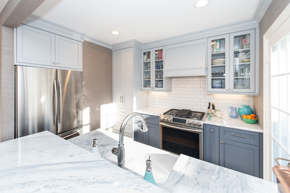 Photo of a transitional single-wall eat-in kitchen in Charleston with a farmhouse sink, white cabinets, white splashback, subway tile splashback, stainless steel appliances, light hardwood floors and a peninsula.