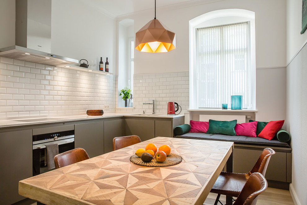 This is an example of a mid-sized contemporary l-shaped eat-in kitchen in Berlin with a single-bowl sink, flat-panel cabinets, grey cabinets, quartzite benchtops, white splashback, subway tile splashback, stainless steel appliances, brown floor, medium hardwood floors, no island and white benchtop.