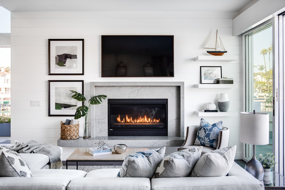 Photo of a mid-sized beach style open concept living room in Los Angeles with white walls, a standard fireplace, a wall-mounted tv, medium hardwood floors, a stone fireplace surround and brown floor.