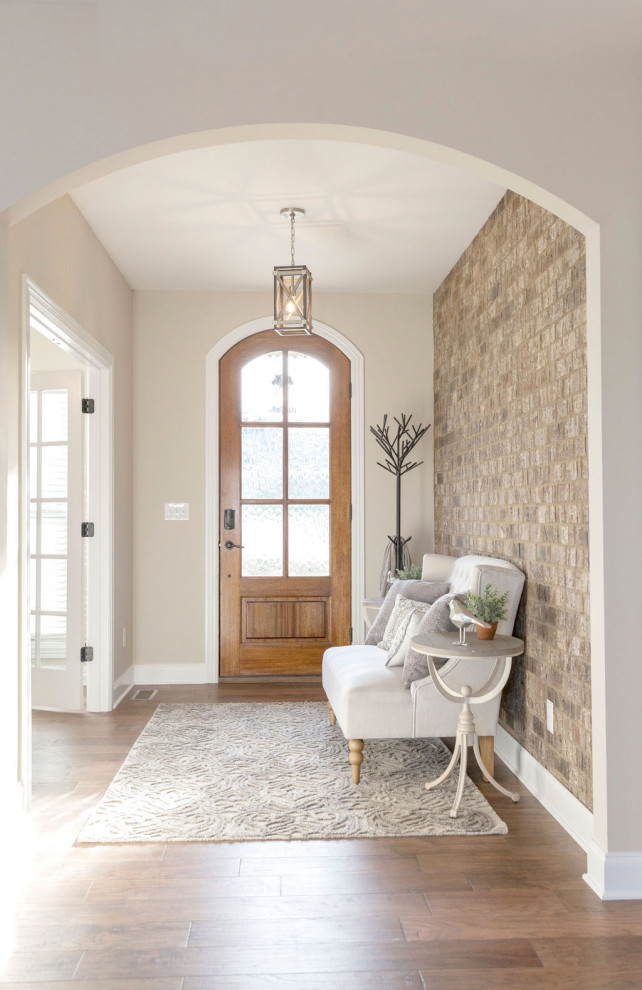 This is an example of a large transitional foyer in Other with beige walls, medium hardwood floors, a single front door, a medium wood front door, brown floor and brick walls.