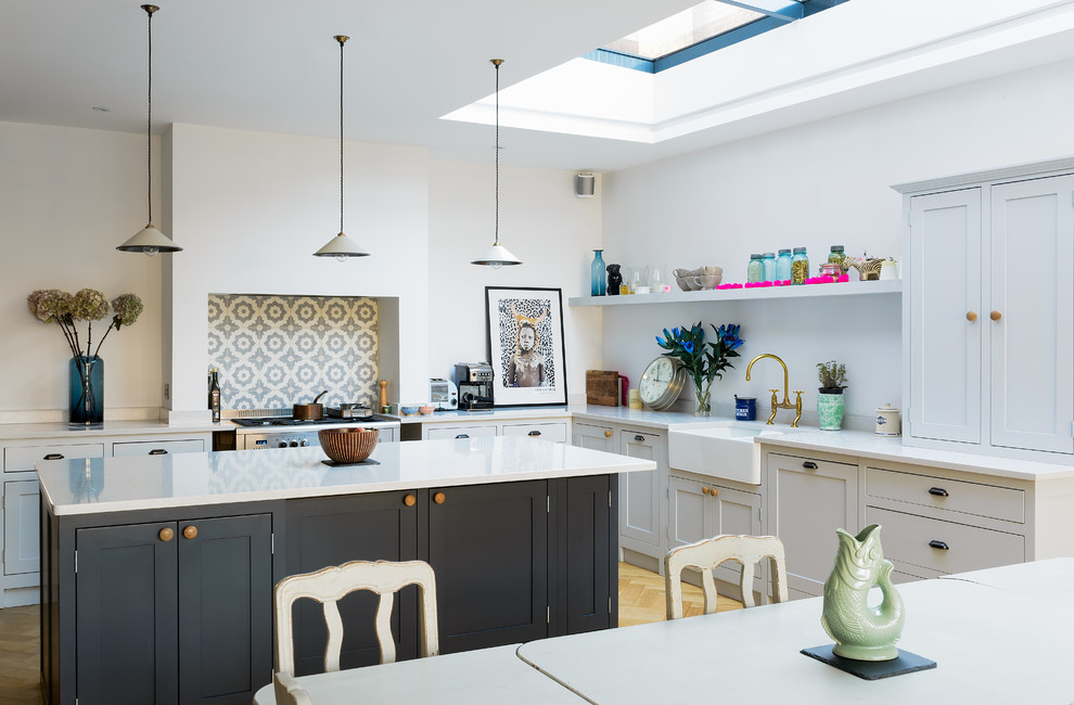 Design ideas for a mid-sized country u-shaped eat-in kitchen in London with a farmhouse sink, shaker cabinets, blue cabinets, white splashback, light hardwood floors and with island.