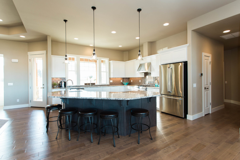 Large transitional l-shaped medium tone wood floor open concept kitchen photo in Seattle with an undermount sink, shaker cabinets, white cabinets, granite countertops, brown backsplash, subway tile backsplash, stainless steel appliances and an island