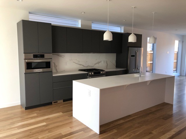 Example of a mid-sized minimalist galley medium tone wood floor and brown floor open concept kitchen design in Denver with an undermount sink, flat-panel cabinets, dark wood cabinets, quartz countertops, white backsplash, porcelain backsplash, stainless steel appliances, an island and white countertops
