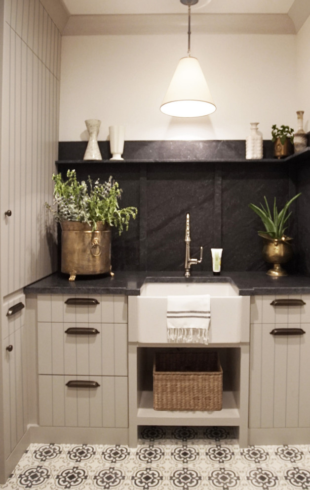 Mid-sized u-shaped dedicated laundry room with a farmhouse sink, flat-panel cabinets, grey cabinets, granite benchtops, black splashback, granite splashback, white walls, a side-by-side washer and dryer and black benchtop.