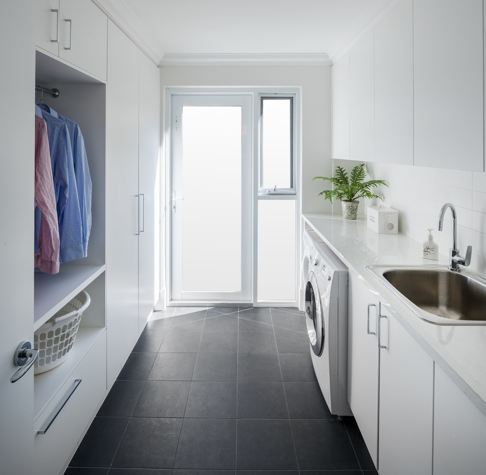 This is an example of a contemporary galley dedicated laundry room in Perth with a drop-in sink, flat-panel cabinets, white cabinets, white walls, a side-by-side washer and dryer, grey floor and white benchtop.