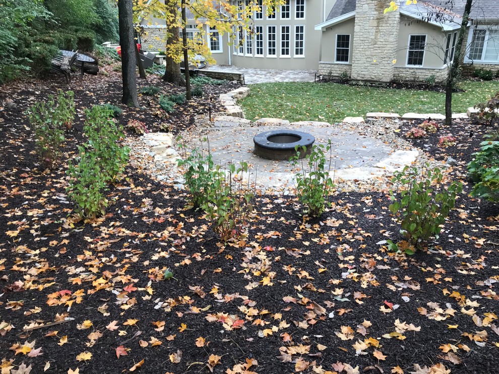This is an example of a large rustic shade backyard concrete paver landscaping with a fire pit for summer.