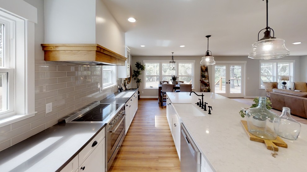 Mid-sized country galley open plan kitchen in Sacramento with a farmhouse sink, shaker cabinets, white cabinets, quartzite benchtops, grey splashback, ceramic splashback, stainless steel appliances, laminate floors, with island, brown floor and white benchtop.