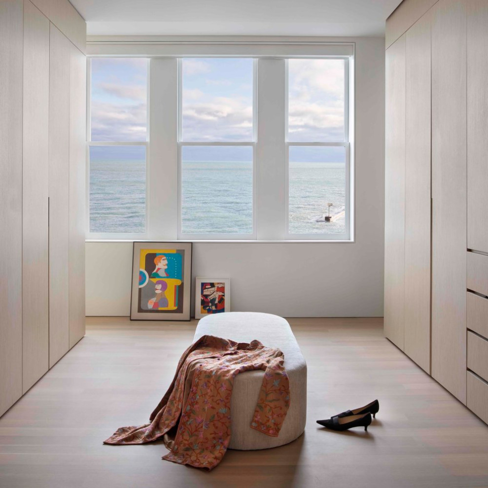 Photo of a mid-sized modern gender-neutral storage and wardrobe in Chicago with flat-panel cabinets, light wood cabinets, light hardwood floors and beige floor.