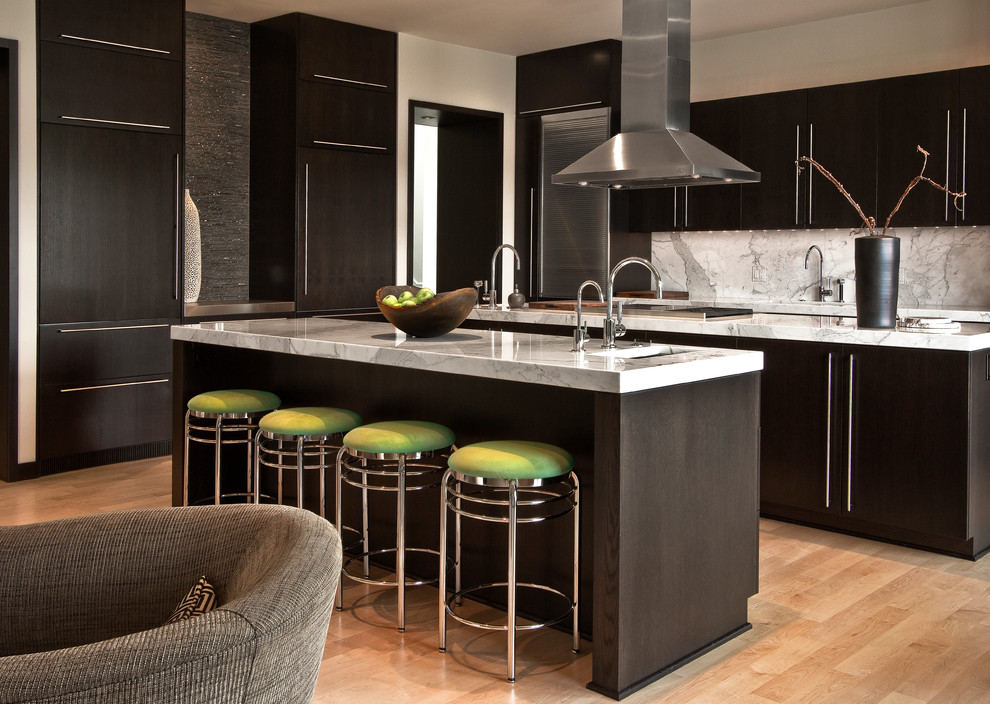 This is an example of a large contemporary galley eat-in kitchen in Detroit with an undermount sink, flat-panel cabinets, dark wood cabinets, marble benchtops, white splashback, stone slab splashback, stainless steel appliances, light hardwood floors and multiple islands.