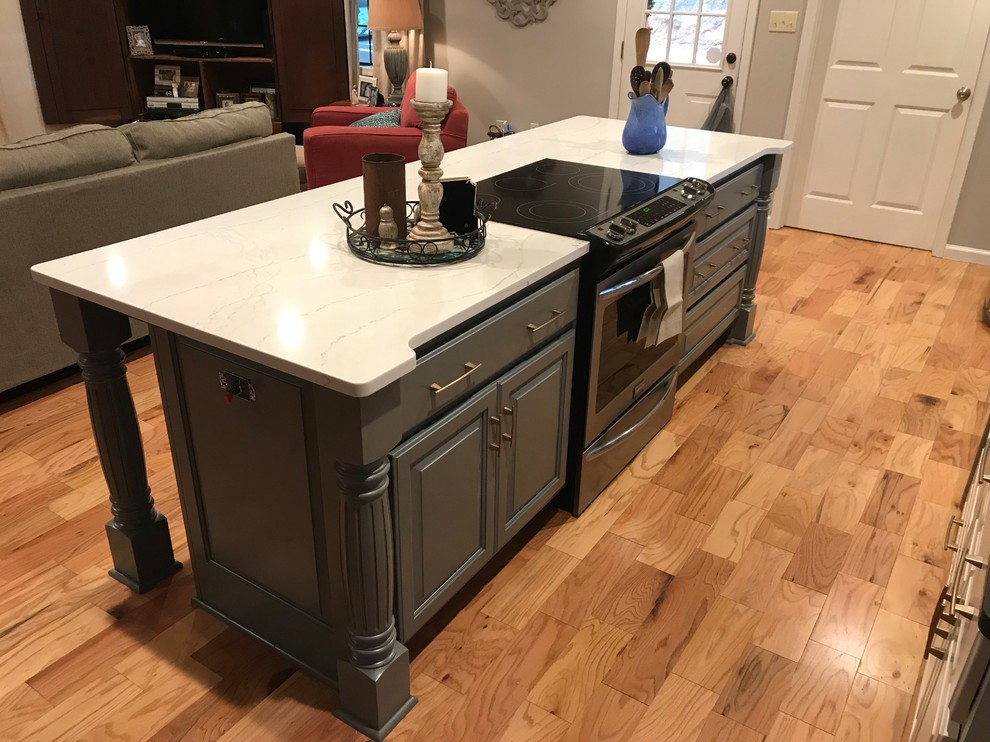 Open concept kitchen - mid-sized transitional l-shaped medium tone wood floor and brown floor open concept kitchen idea with an undermount sink, raised-panel cabinets, white cabinets, white backsplash, stainless steel appliances, an island and white countertops