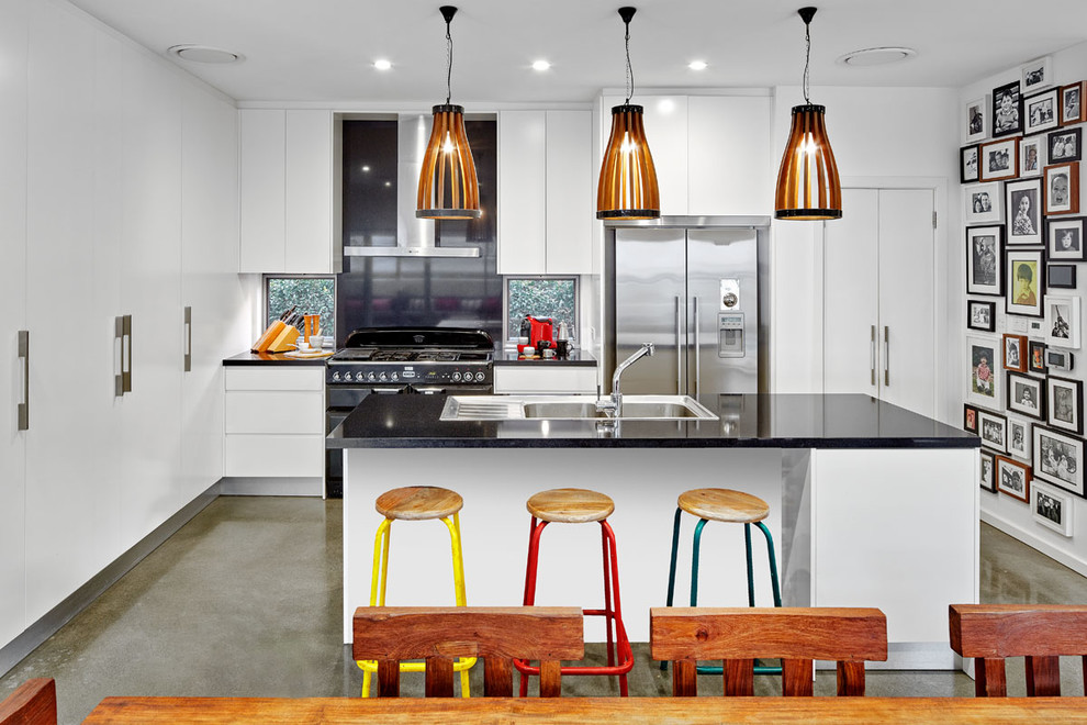 Inspiration for a large contemporary l-shaped kitchen in Sydney with a double-bowl sink, flat-panel cabinets, quartz benchtops, black splashback, black appliances, concrete floors and with island.