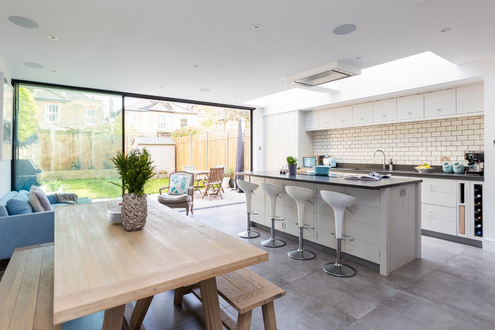This is an example of a contemporary kitchen in London with flat-panel cabinets, white cabinets, white splashback, subway tile splashback and with island.