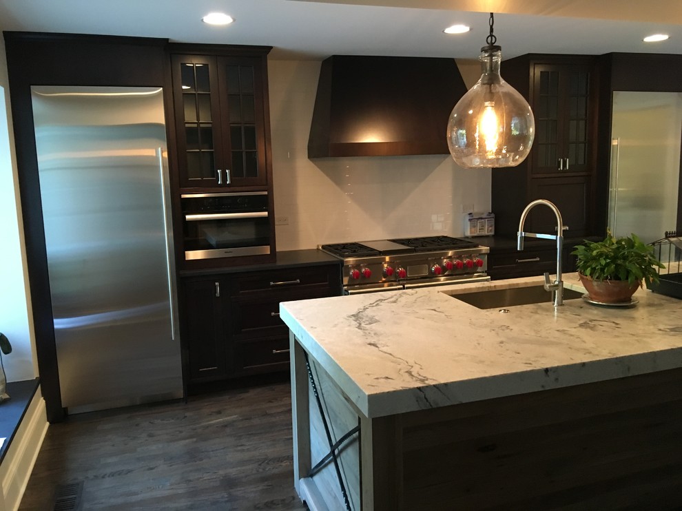 Photo of a mid-sized traditional single-wall eat-in kitchen in Chicago with an undermount sink, flat-panel cabinets, dark wood cabinets, marble benchtops, white splashback, ceramic splashback, stainless steel appliances, dark hardwood floors, with island, black floor and white benchtop.