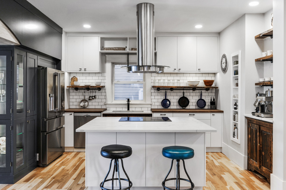 Arts and crafts u-shaped kitchen in Calgary with an undermount sink, flat-panel cabinets, white cabinets, wood benchtops, white splashback, subway tile splashback, stainless steel appliances, light hardwood floors, with island, beige floor and brown benchtop.
