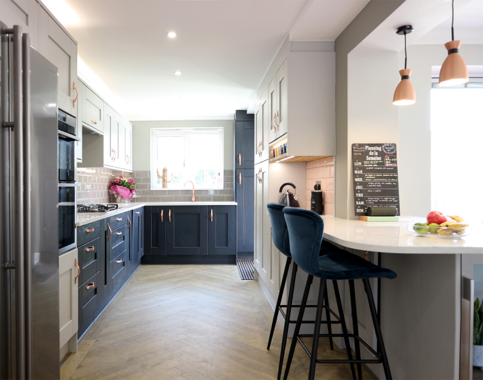 Photo of a mid-sized modern u-shaped eat-in kitchen in Hertfordshire with a farmhouse sink, shaker cabinets, grey cabinets, quartzite benchtops, grey splashback, subway tile splashback, panelled appliances, vinyl floors, a peninsula, brown floor and white benchtop.