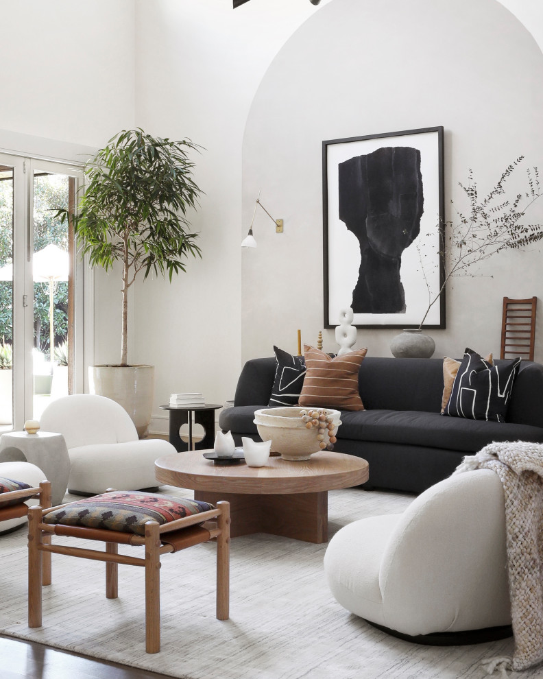 Idée de décoration pour un grand salon blanc et bois design ouvert avec un mur blanc, un sol en bois brun, un téléviseur dissimulé, canapé noir et un plafond voûté.