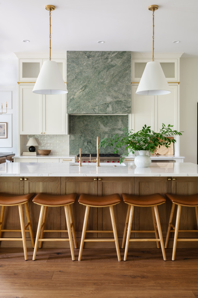 Transitional galley medium tone wood floor and brown floor kitchen photo with an undermount sink, shaker cabinets, beige cabinets, white backsplash, stainless steel appliances, an island and white countertops