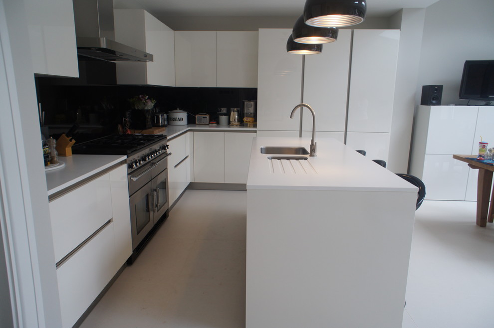 This is an example of a mid-sized modern l-shaped open plan kitchen in London with a double-bowl sink, flat-panel cabinets, white cabinets, solid surface benchtops, black splashback, glass sheet splashback, stainless steel appliances and with island.