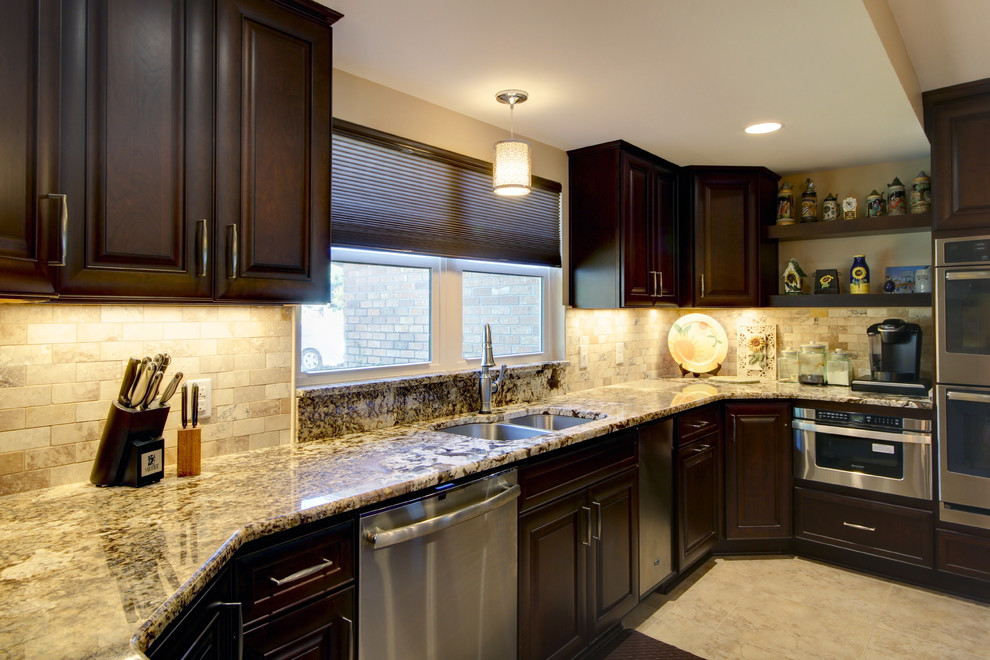 Eat-in kitchen - large transitional l-shaped porcelain tile eat-in kitchen idea in Miami with an undermount sink, raised-panel cabinets, dark wood cabinets, granite countertops, beige backsplash, stone tile backsplash, stainless steel appliances and an island