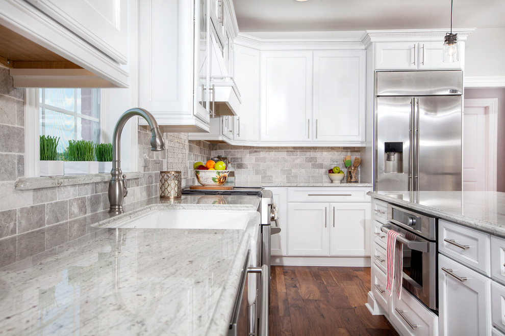 Inspiration for a traditional l-shaped eat-in kitchen in Chicago with a farmhouse sink, recessed-panel cabinets, white cabinets, granite benchtops, grey splashback, stone tile splashback, stainless steel appliances, medium hardwood floors and with island.