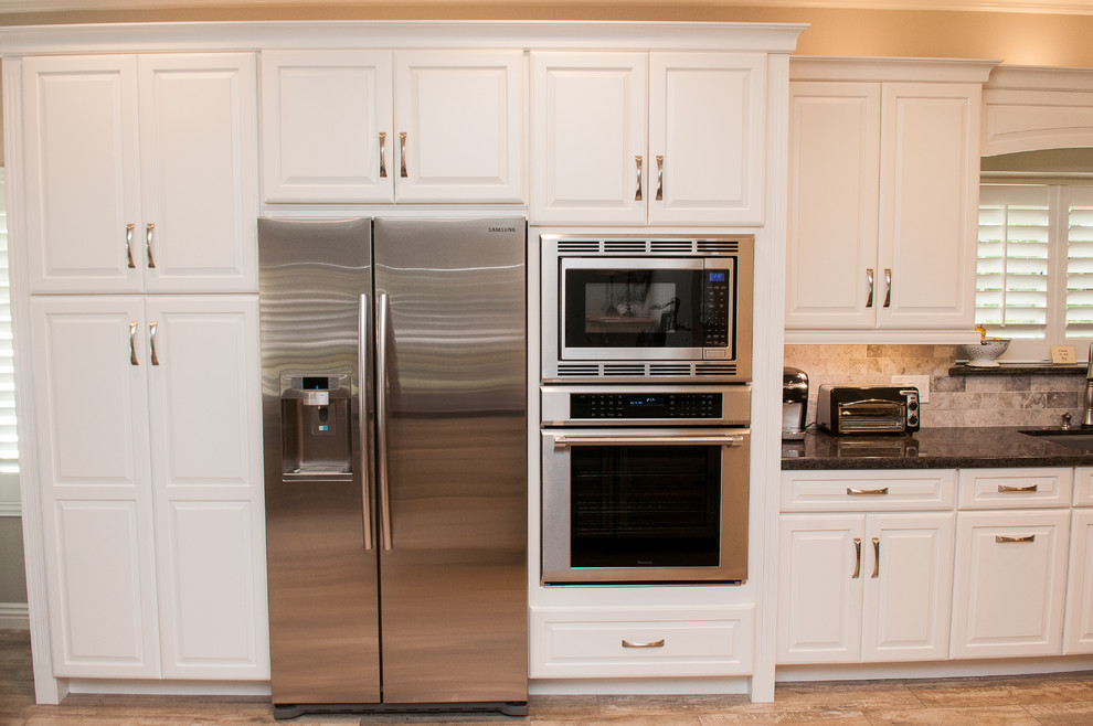 Mid-sized transitional galley porcelain tile and beige floor enclosed kitchen photo with a triple-bowl sink, raised-panel cabinets, white cabinets, granite countertops, beige backsplash, porcelain backsplash, stainless steel appliances and a peninsula