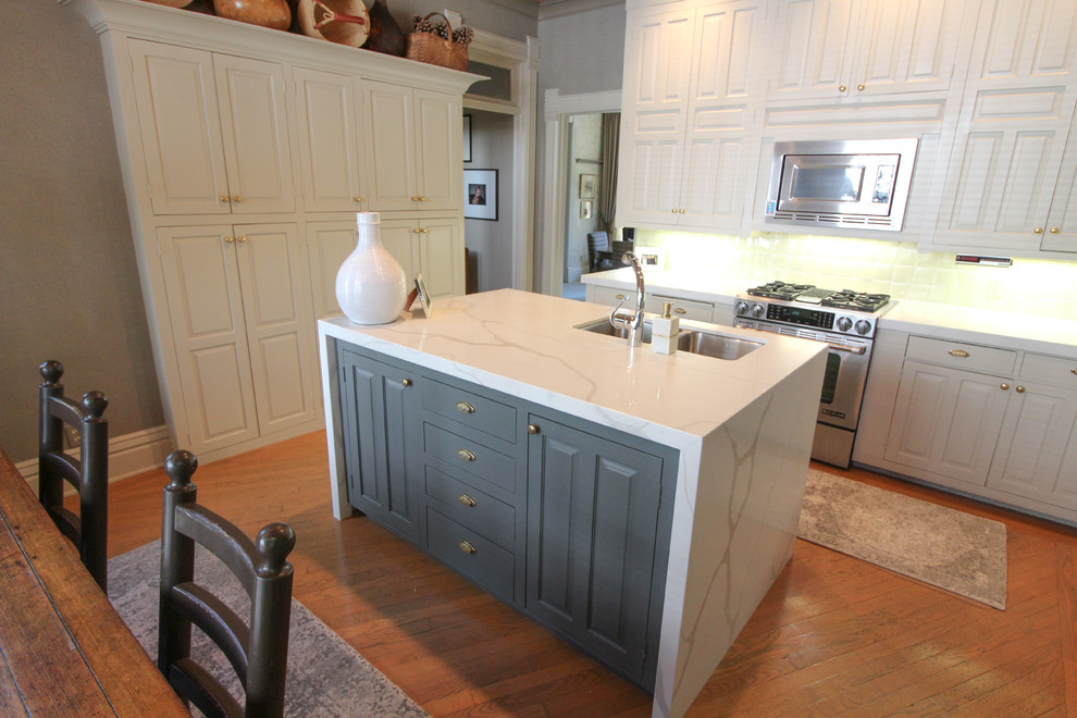 Transitional medium tone wood floor and brown floor kitchen photo with an undermount sink, raised-panel cabinets, white cabinets, quartz countertops, white backsplash, ceramic backsplash, stainless steel appliances, an island and white countertops