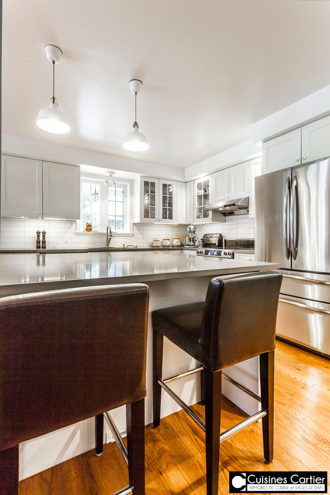 Inspiration for a large transitional medium tone wood floor eat-in kitchen remodel in Montreal with a double-bowl sink, shaker cabinets, white cabinets, quartzite countertops, white backsplash, ceramic backsplash, stainless steel appliances and an island