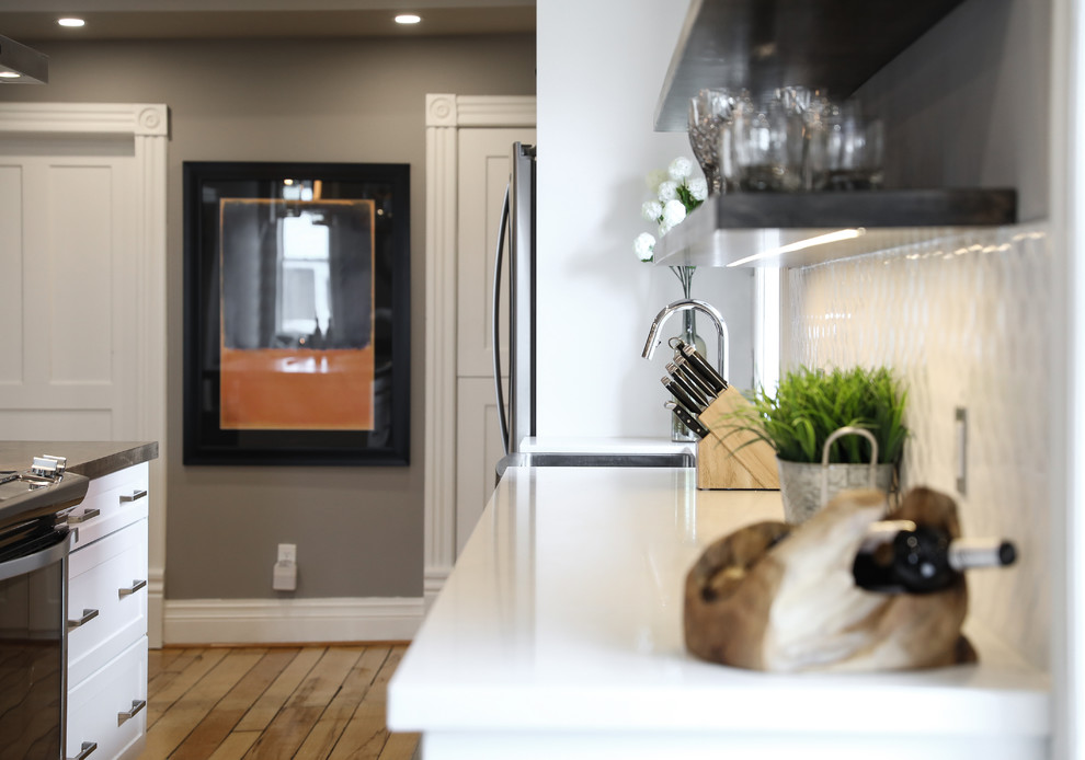 Inspiration for a mid-sized transitional single-wall medium tone wood floor and brown floor eat-in kitchen remodel with a farmhouse sink, shaker cabinets, white cabinets, white backsplash, stainless steel appliances, an island and white countertops