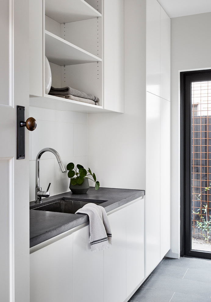 Photo of a mid-sized contemporary galley dedicated laundry room in Melbourne with an undermount sink, white cabinets, concrete benchtops, white splashback, porcelain splashback, white walls, porcelain floors and grey benchtop.