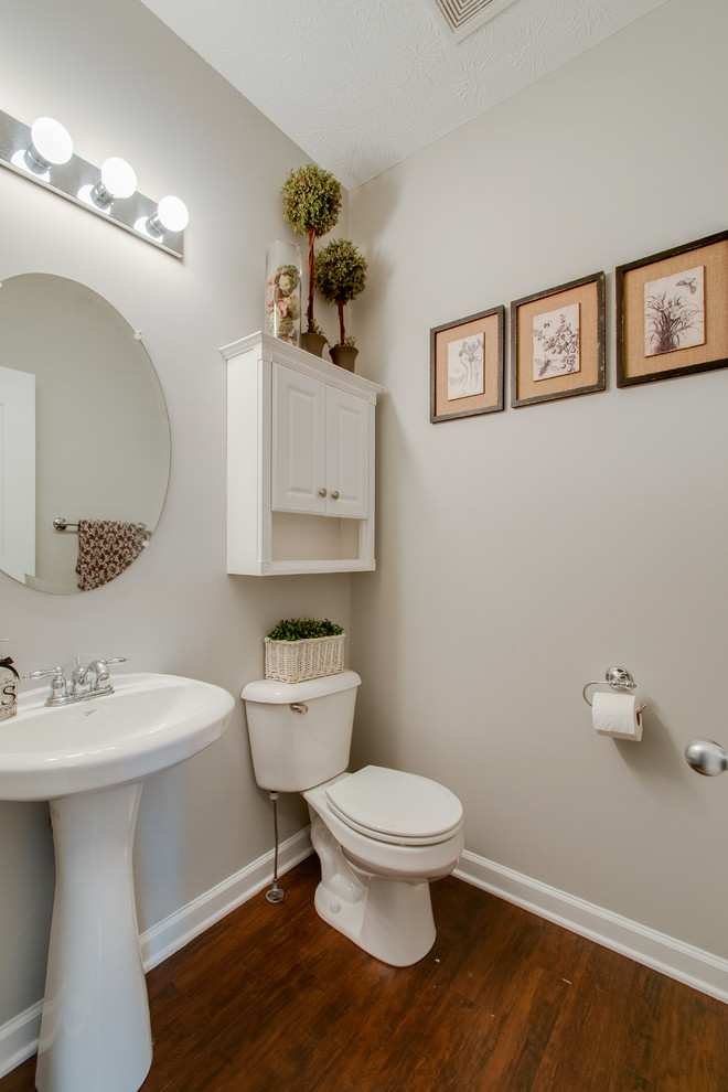 This is an example of a small country powder room in Nashville with a two-piece toilet, grey walls, medium hardwood floors, a pedestal sink and brown floor.