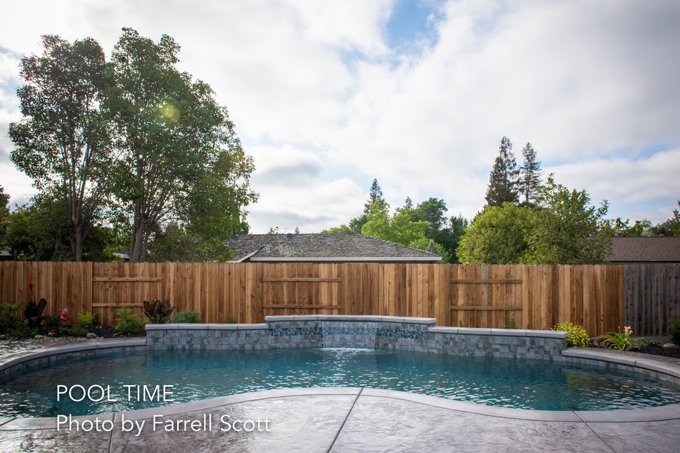 This is an example of a mid-sized modern backyard kidney-shaped pool in Sacramento with a water feature and stamped concrete.