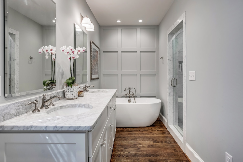 Inspiration for a transitional bathroom in Richmond with shaker cabinets, white cabinets, a freestanding tub, medium hardwood floors, marble benchtops, brown floor, a hinged shower door and grey benchtops.