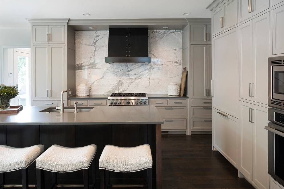 Large transitional l-shaped open plan kitchen in Minneapolis with an undermount sink, shaker cabinets, grey cabinets, marble splashback, stainless steel appliances, dark hardwood floors, with island, quartzite benchtops, white splashback and brown floor.