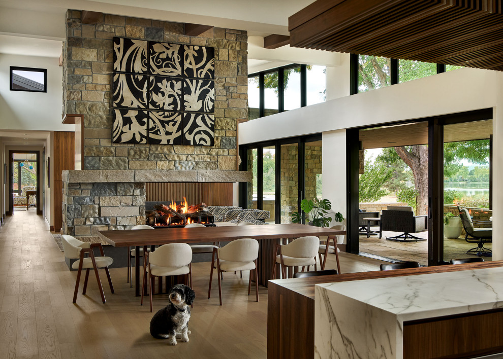 Example of a large trendy medium tone wood floor, brown floor and vaulted ceiling great room design in Denver with white walls, a two-sided fireplace and a stone fireplace