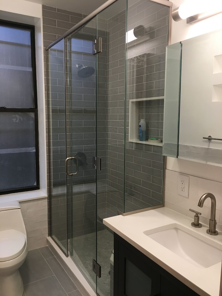 This is an example of a small contemporary 3/4 bathroom in New York with flat-panel cabinets, dark wood cabinets, an alcove shower, a one-piece toilet, gray tile, white tile, subway tile, grey walls, porcelain floors, an undermount sink, quartzite benchtops, grey floor and a hinged shower door.