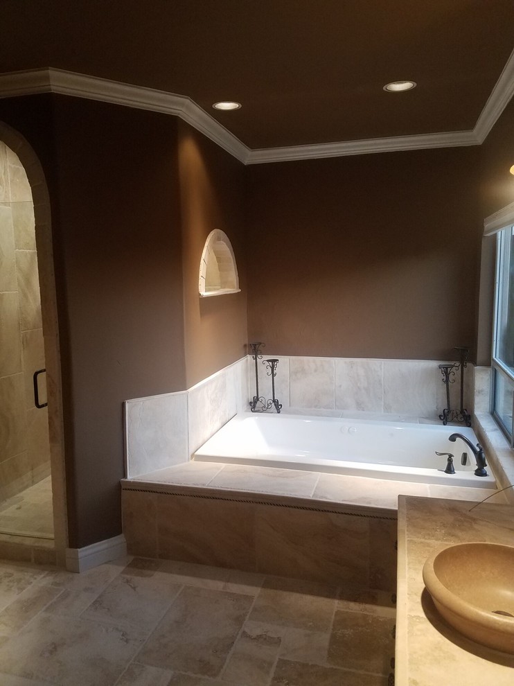 Photo of a large traditional master bathroom in Sacramento with raised-panel cabinets, dark wood cabinets, a drop-in tub, an alcove shower, beige tile, ceramic tile, brown walls, travertine floors, a vessel sink, beige floor, a hinged shower door and beige benchtops.